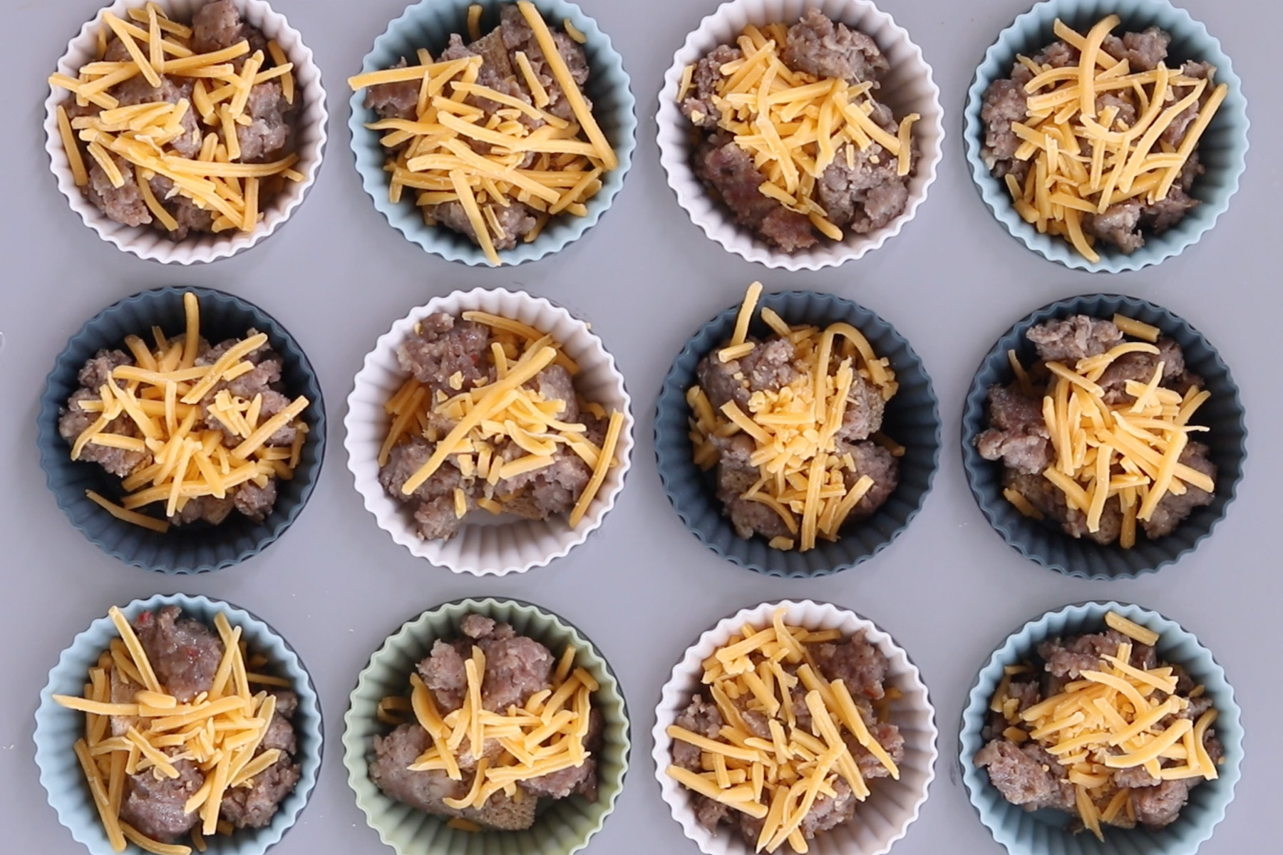 Silicone muffin cups filled with bread, cooked sausage, and shredded cheddar for baked egg muffins.