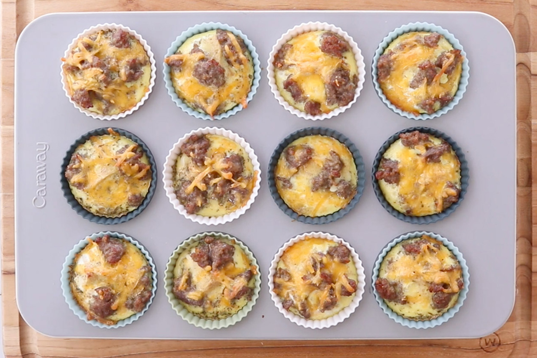 Baked sausage and cheese egg muffins cooling in silicone liners inside a muffin pan before freezing.
