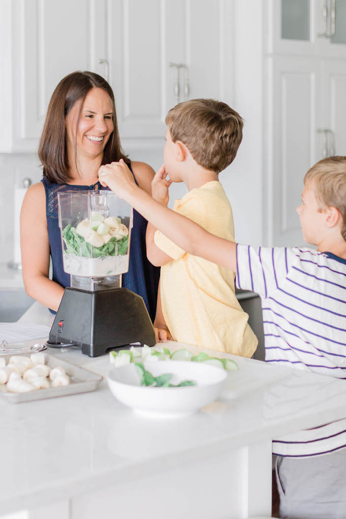 Go Green Spinach Apple Smoothie ingredients being put into the blender jar by 2 young boys and a brunette woman.