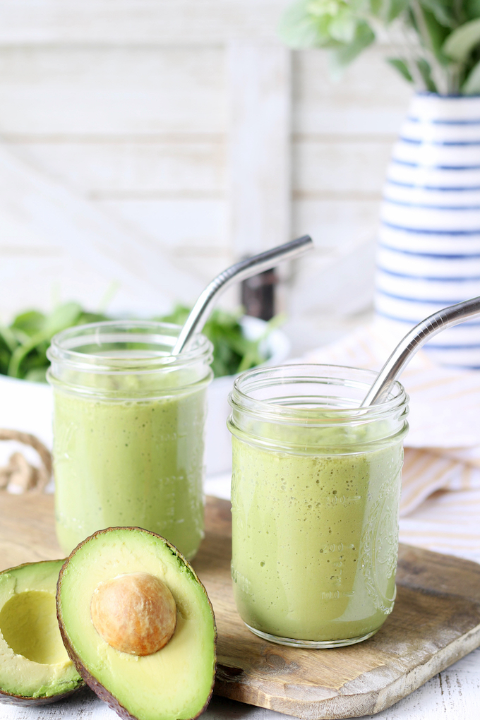 Go Green Spinach Apple Smoothies inside 2 mason jars with silver metal straws. Avocado, spinach and a small green plant are in the background.