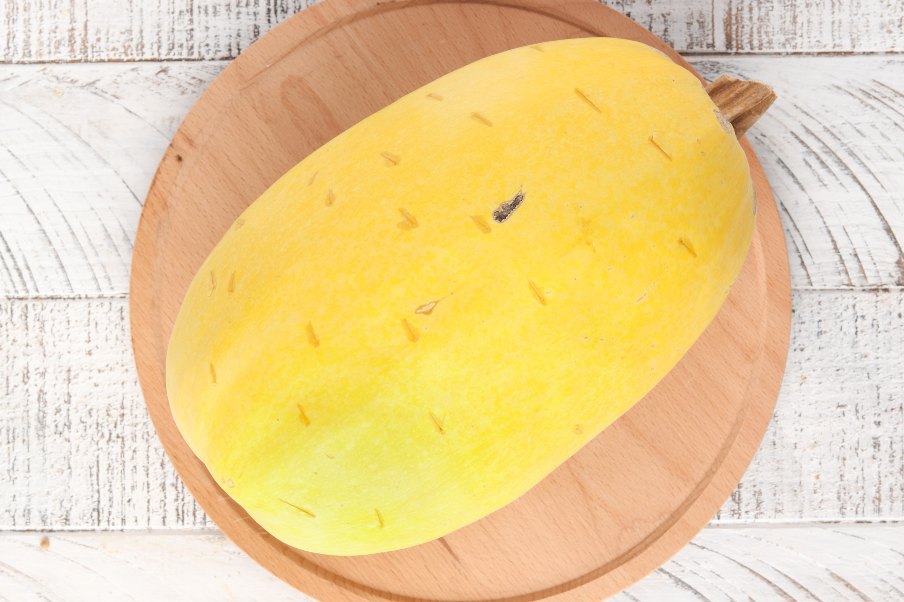 Whole spaghetti squash that has been poked with holes on a wood cutting board.
