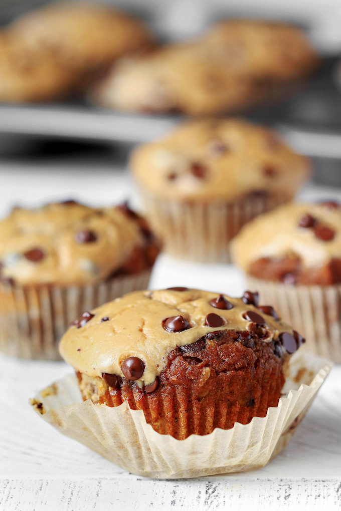 A partially unwrapped Whole Wheat Pumpkin Cheesecake Muffin on a white wooden background.