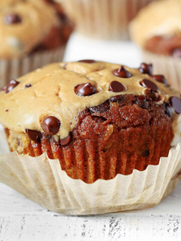 Close-up of a pumpkin cheesecake muffin with chocolate chips, unwrapped from its paper liner, showing a golden top and moist texture inside.