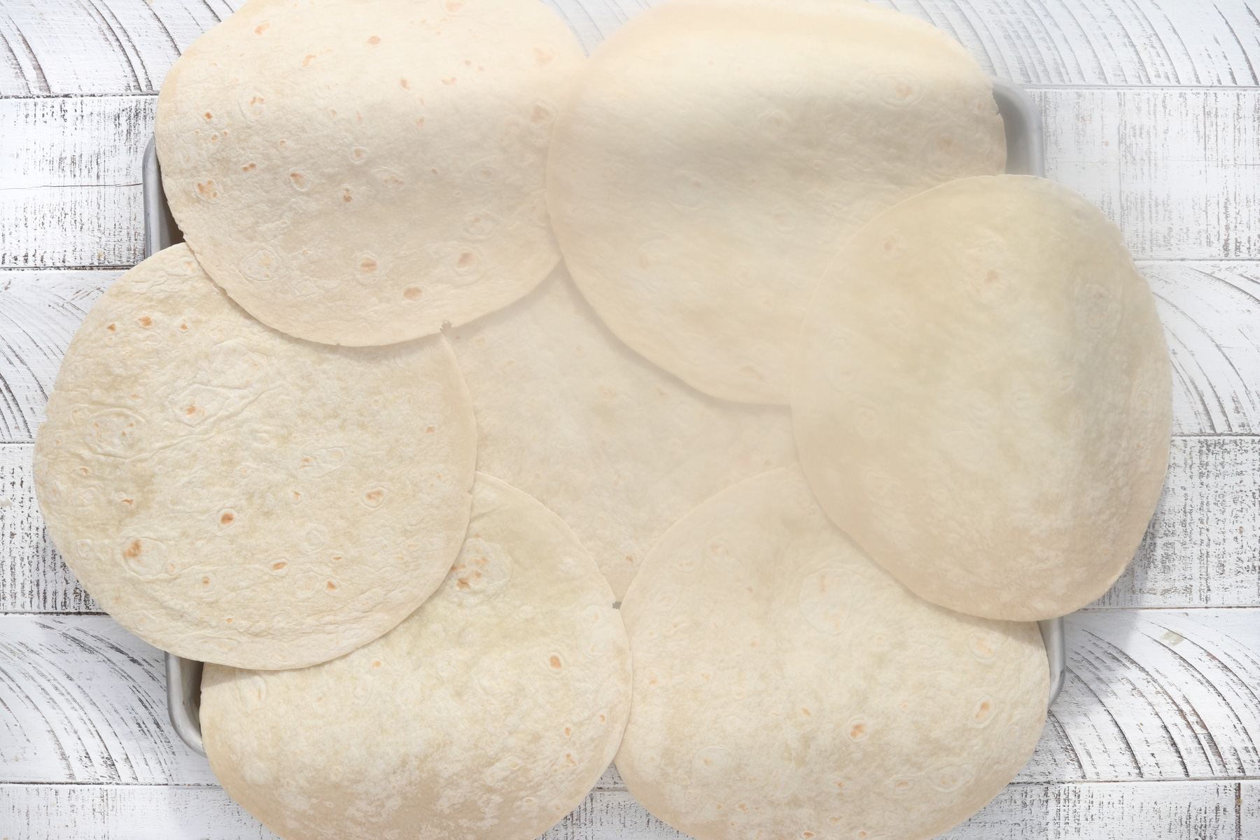 Baking sheet covered with overlapping flour tortillas arranged in a single layer.