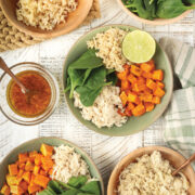 Honey Lime Chicken Macro Bowls on a white table surrounded by brown rice, sweet potatoes, dressing and chicken.