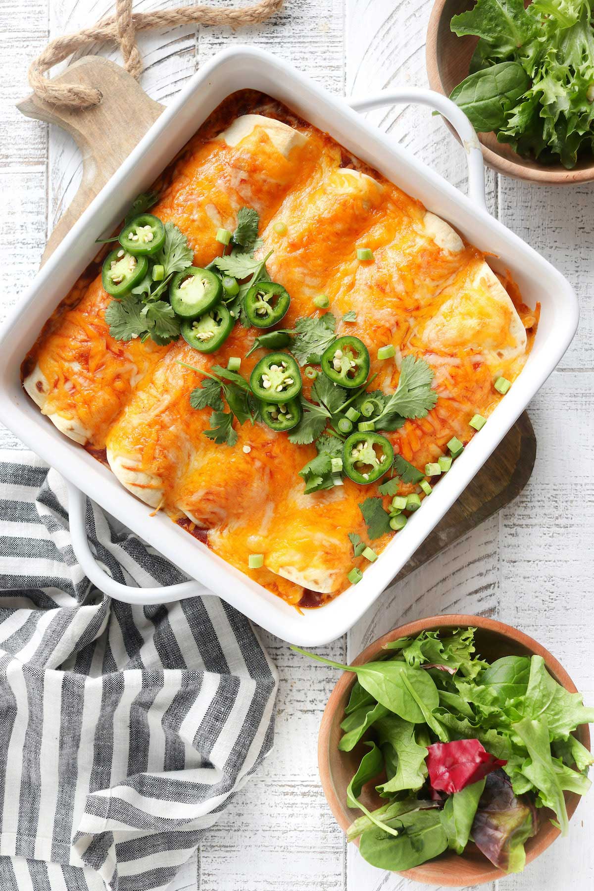 White baking dish filled with chicken enchiladas and topped with cilantro and jalapeños.