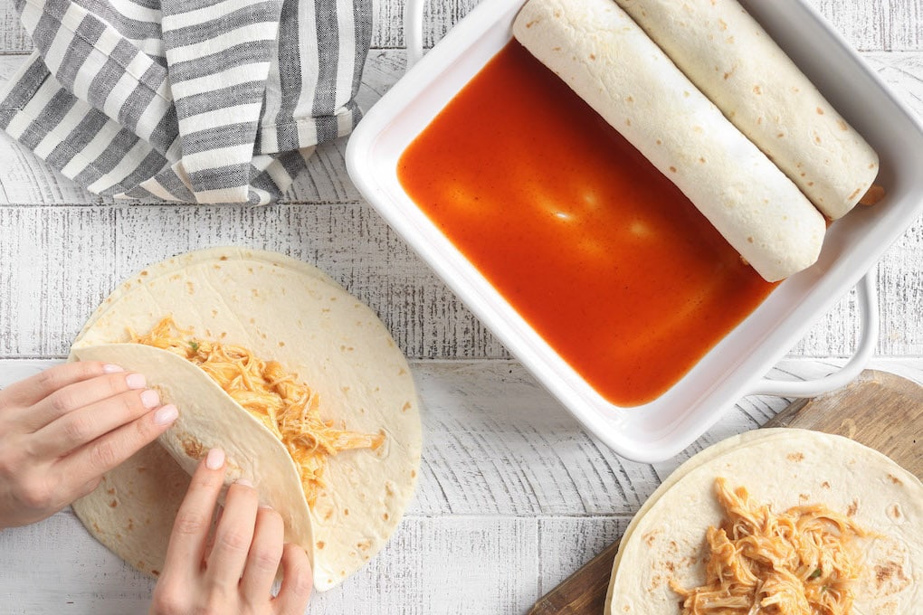 Step 4: An image of a woman's hands rolling a flour tortilla with chicken enchilada filling.