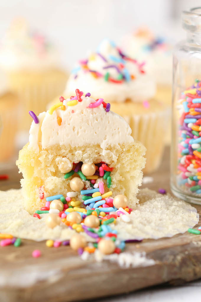 Vanilla Sprinkle Filled Piñata Cupcake  with white buttercream icing on a wood surface.