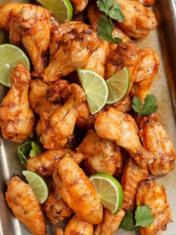 Grilled Hot Honey Chicken Wings arranged on a sheet pan with lime slices.