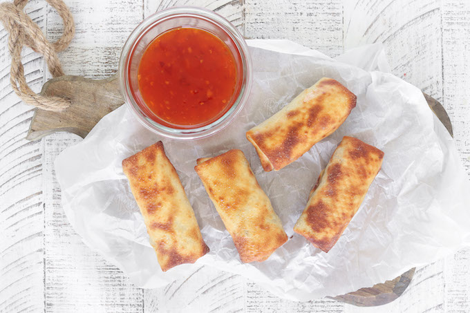 Air Fryer Egg Rolls cooling on a wood platter with sweet chili dipping sauce.
