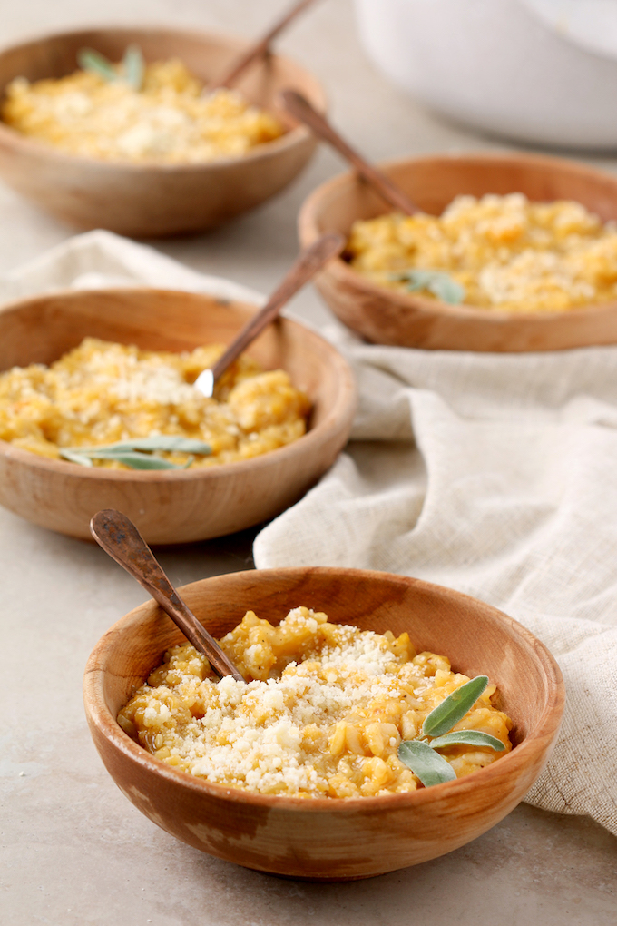4 wooden bowls filled with butternut squash risotto. Each bowl is topped with a sprig of sage.