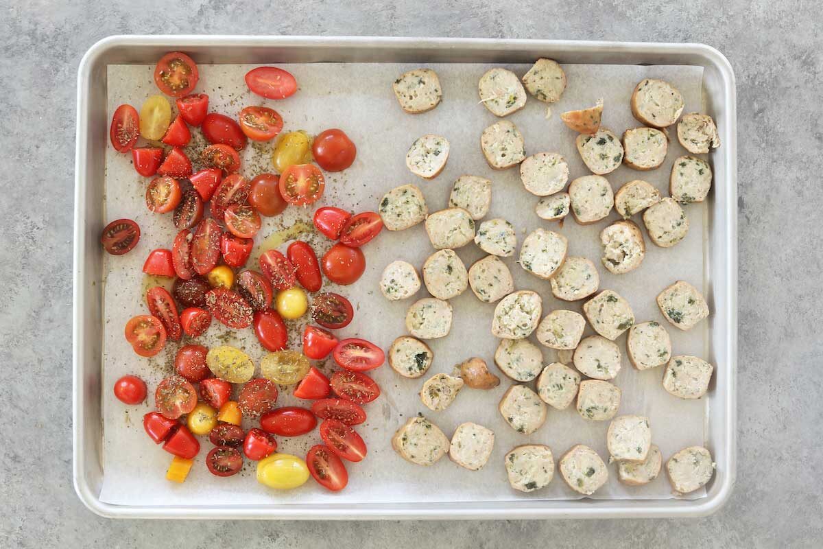 Step 1: grape tomatoes and chicken sausage arrange into a single layer on a sheet pan. The tomatoes are topped with olive oil and Italian seasoning.