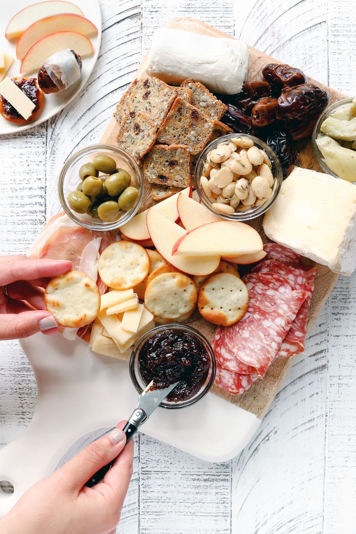 Charcuterie Board containing smoked meats, nuts, cheeses, artichokes, olives, fig butter crackers and apples.