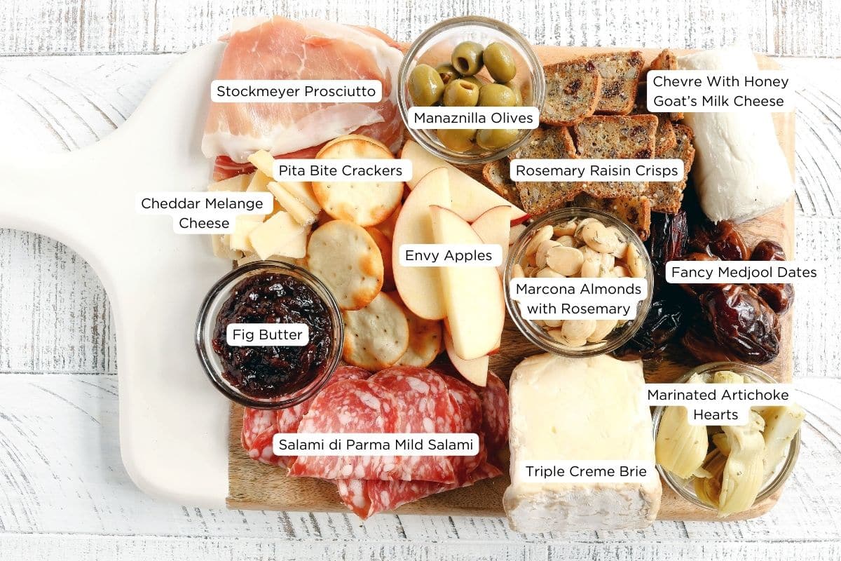 Basic Charcuterie Board containing smoked meats, nuts, cheeses, artichokes, olives, fig butter crackers and apples from trader joes. All ingredients are labeled.