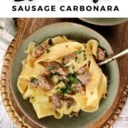 Bowl of 20-minute sausage carbonara made with wide pappardelle noodles, browned Italian sausage, and fresh parsley, served in a green bowl on a wooden tray.