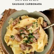Bowl of 20-minute sausage carbonara made with wide pappardelle noodles, browned Italian sausage, and fresh parsley, served in a green bowl on a wooden tray.