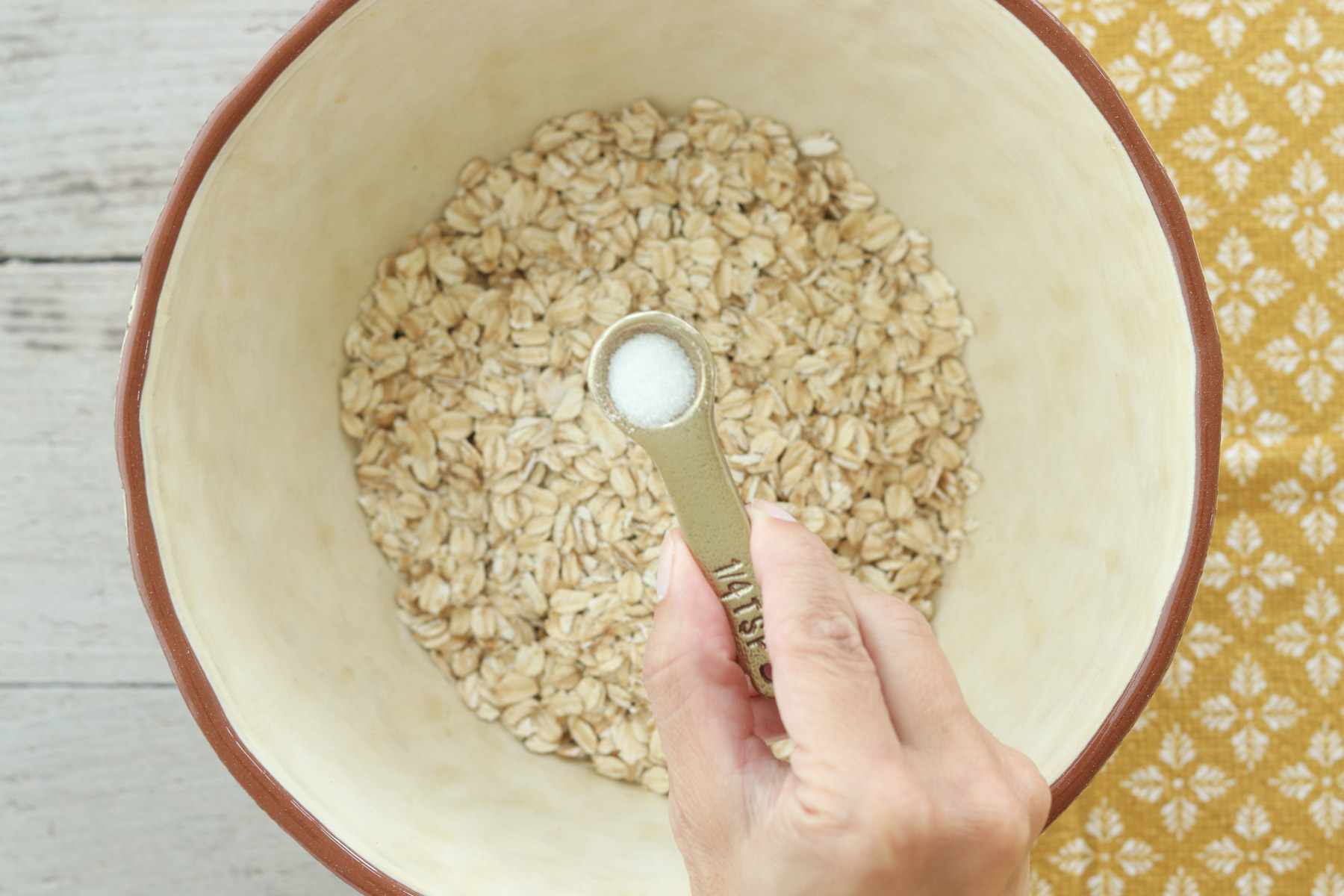 Hand adding salt to rolled oats in a mixing bowl for no-bake peanut butter power balls.