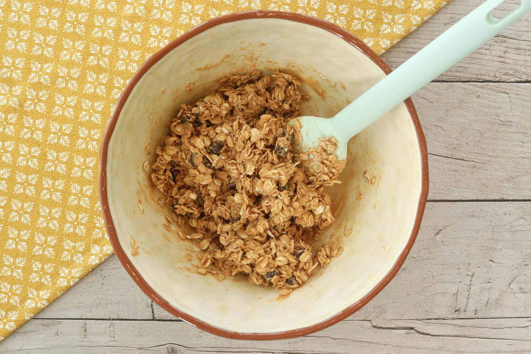 Overhead view of the mixed no-bake peanut butter power ball mixture with oats and chocolate chips in a bowl with a spatula.