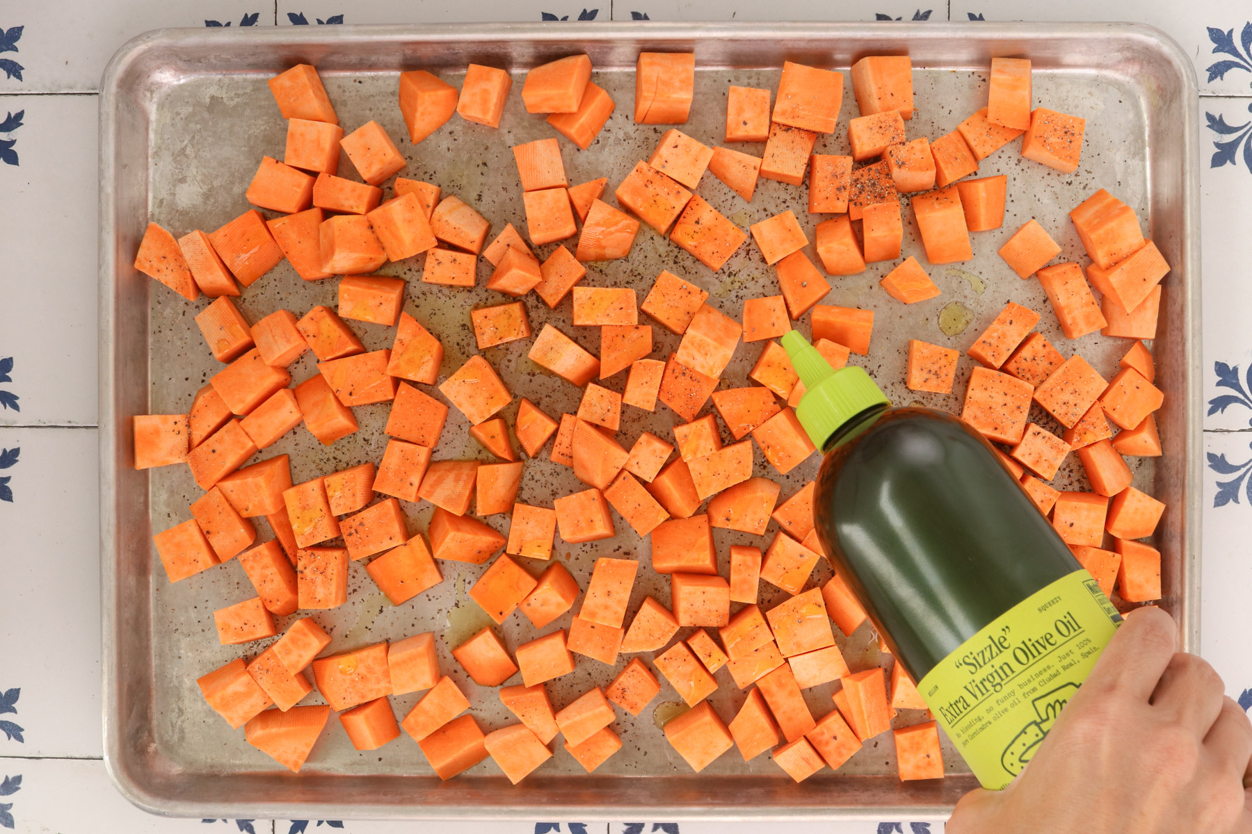 Cubed sweet potatoes seasoned with salt and pepper and drizzled with olive oil on a sheet pan before roasting.