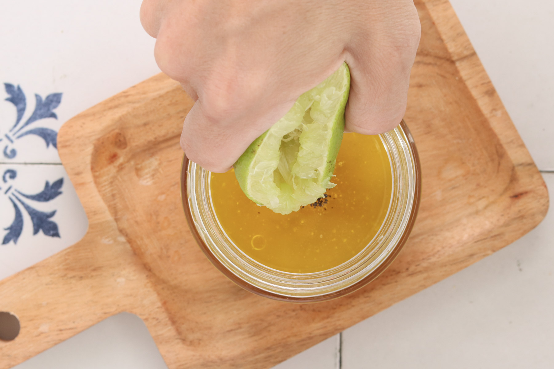 Fresh lime juice being squeezed into a jar of honey-lime dressing for chicken sausage sweet potato bowls.