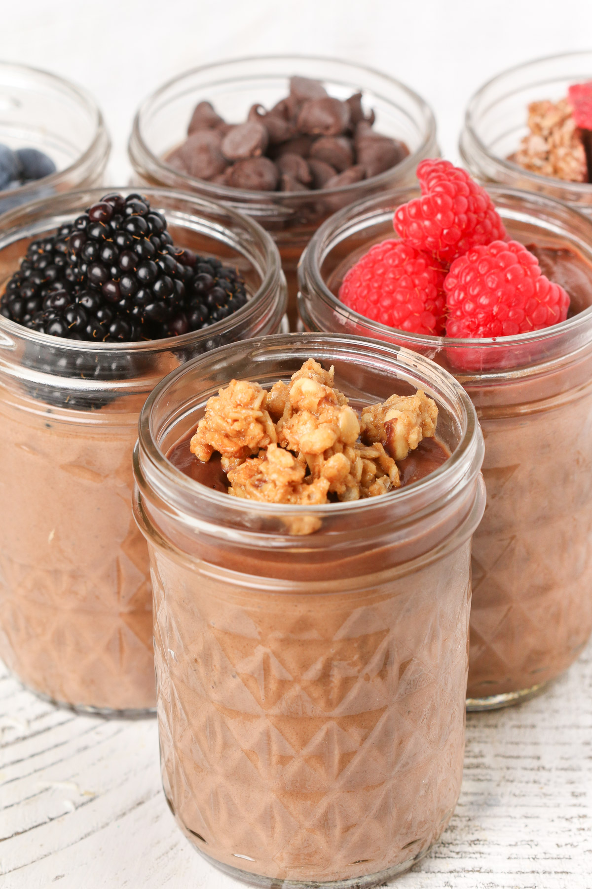 Chocolate Blended Overnight Oats in mason jars with various toppings - berries, granola and chocolate chips.