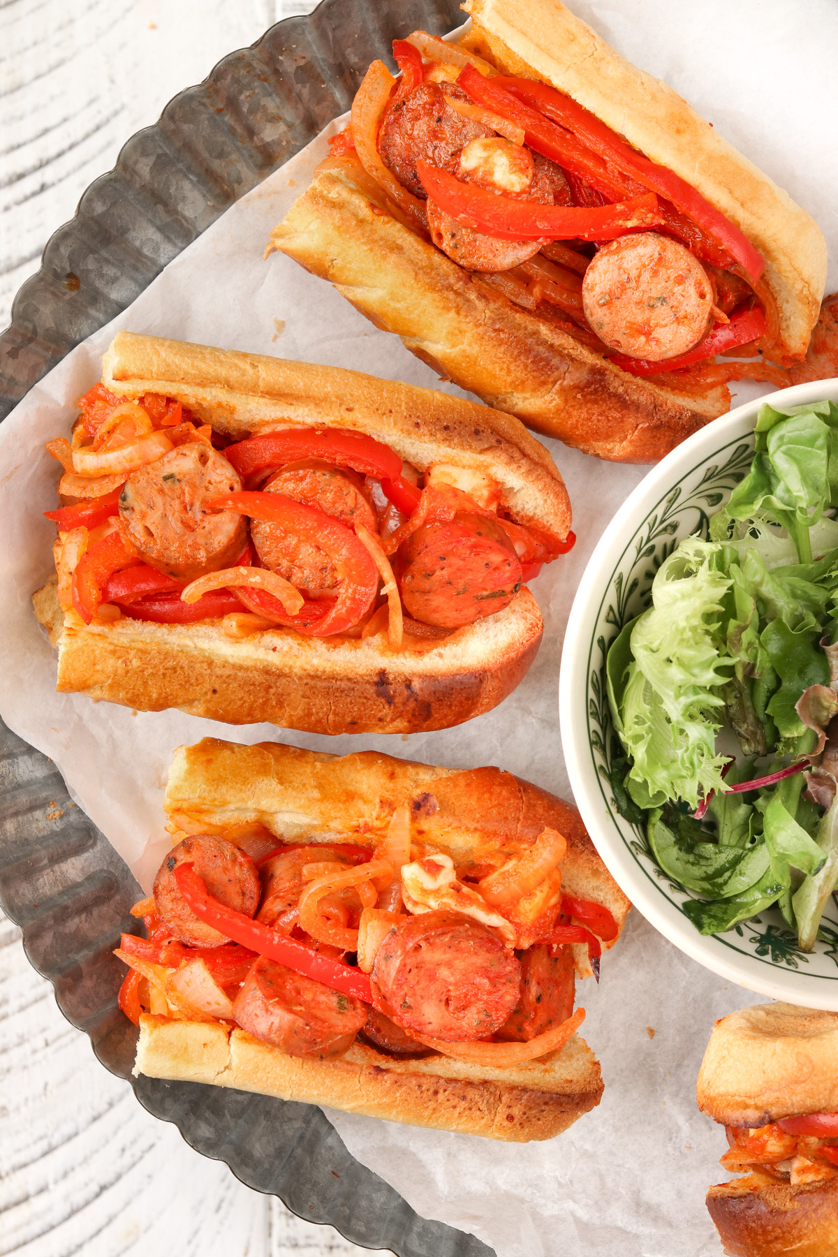 Italian Sausage on a bun being served with a side salad on a silver plate.