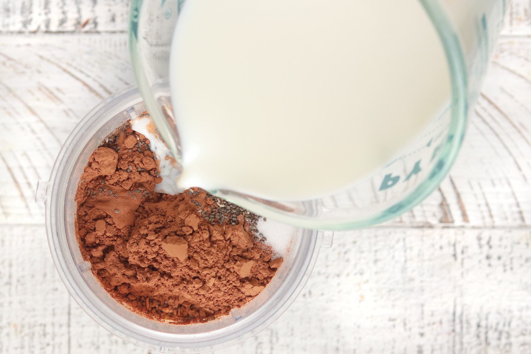 Step 1 - Chocolate Blended Overnight Oat ingredients in a blender. Milk is being added from upper right hand corner.