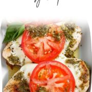 Overhead view of baked pesto chicken breasts topped with melted mozzarella, fresh tomato slices, and basil, arranged in a white ceramic baking dish.