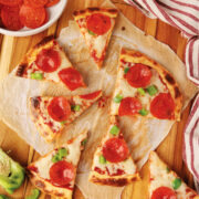 High Protein Cottage Cheese Pizza crust topped with cheese and pepperoni. A hand is reaching into the image to grab a slice.