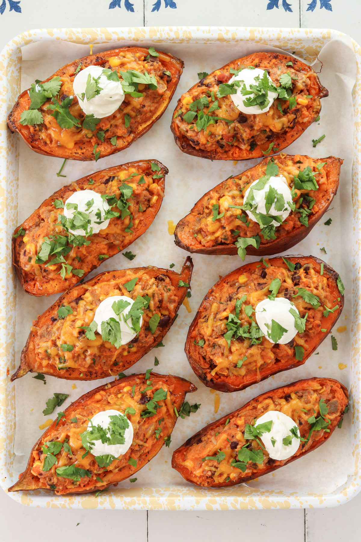 Loaded Mexican sweet potatoes stuffed with ground beef, black beans, corn, and cheese, topped with sour cream and cilantro.