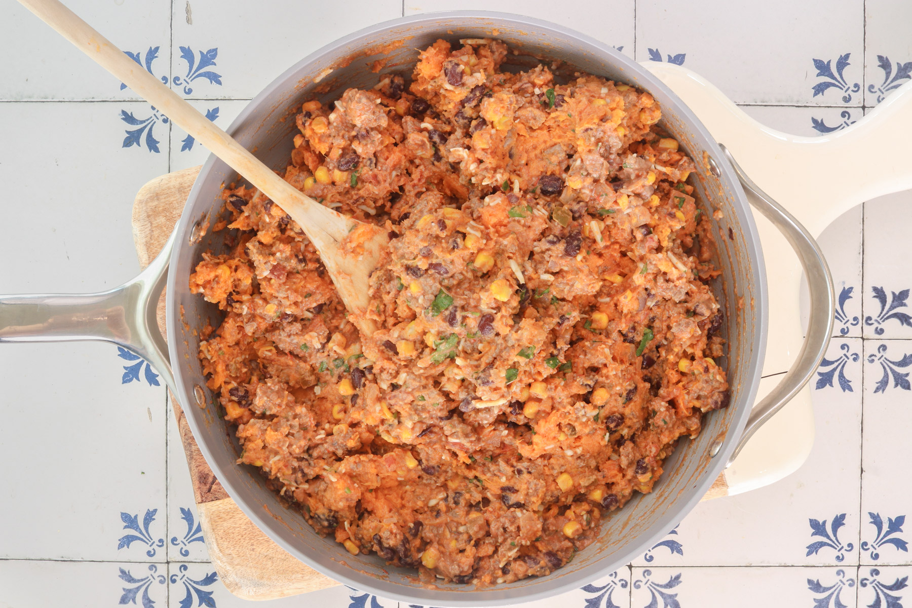 Mexican sweet potato filling with ground beef, black beans, corn, and cheese mixed together in a skillet.