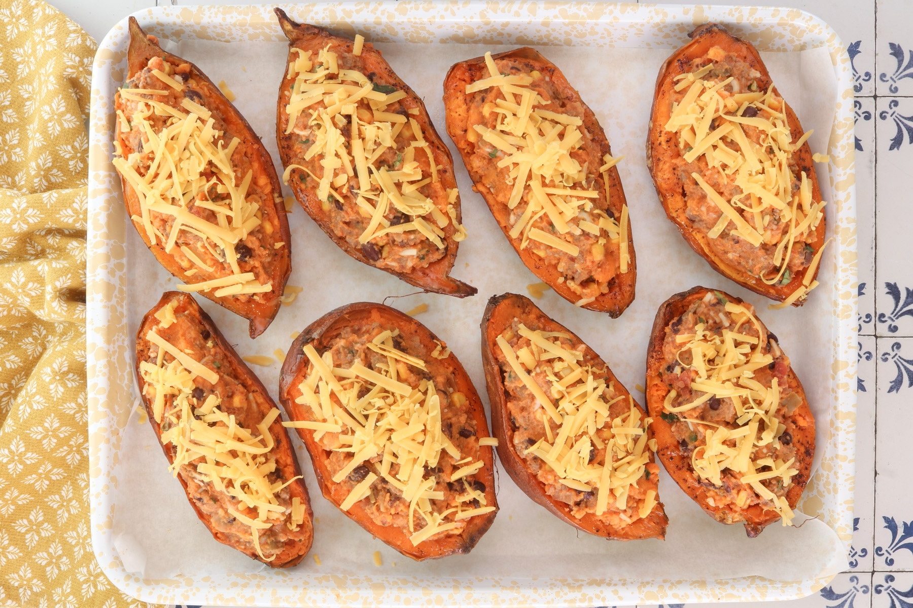 Loaded Mexican sweet potatoes filled with ground beef, black beans, corn, and cheese, topped with shredded cheddar before baking.