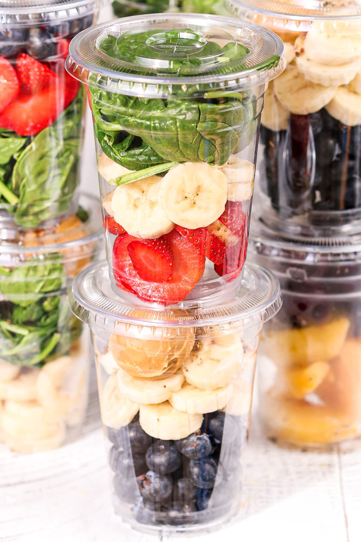 Frozen smoothie packs in clear cups layered with strawberries, bananas, spinach, and blueberries for easy meal prep