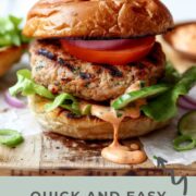 Juicy Asian turkey burger on a toasted brioche bun with lettuce, tomato slices, red onion, and creamy sriracha mayo dripping down the side.