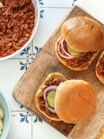 Homemade sloppy joe sandwiches topped with pickles and red onion, served with potato chips and coleslaw.