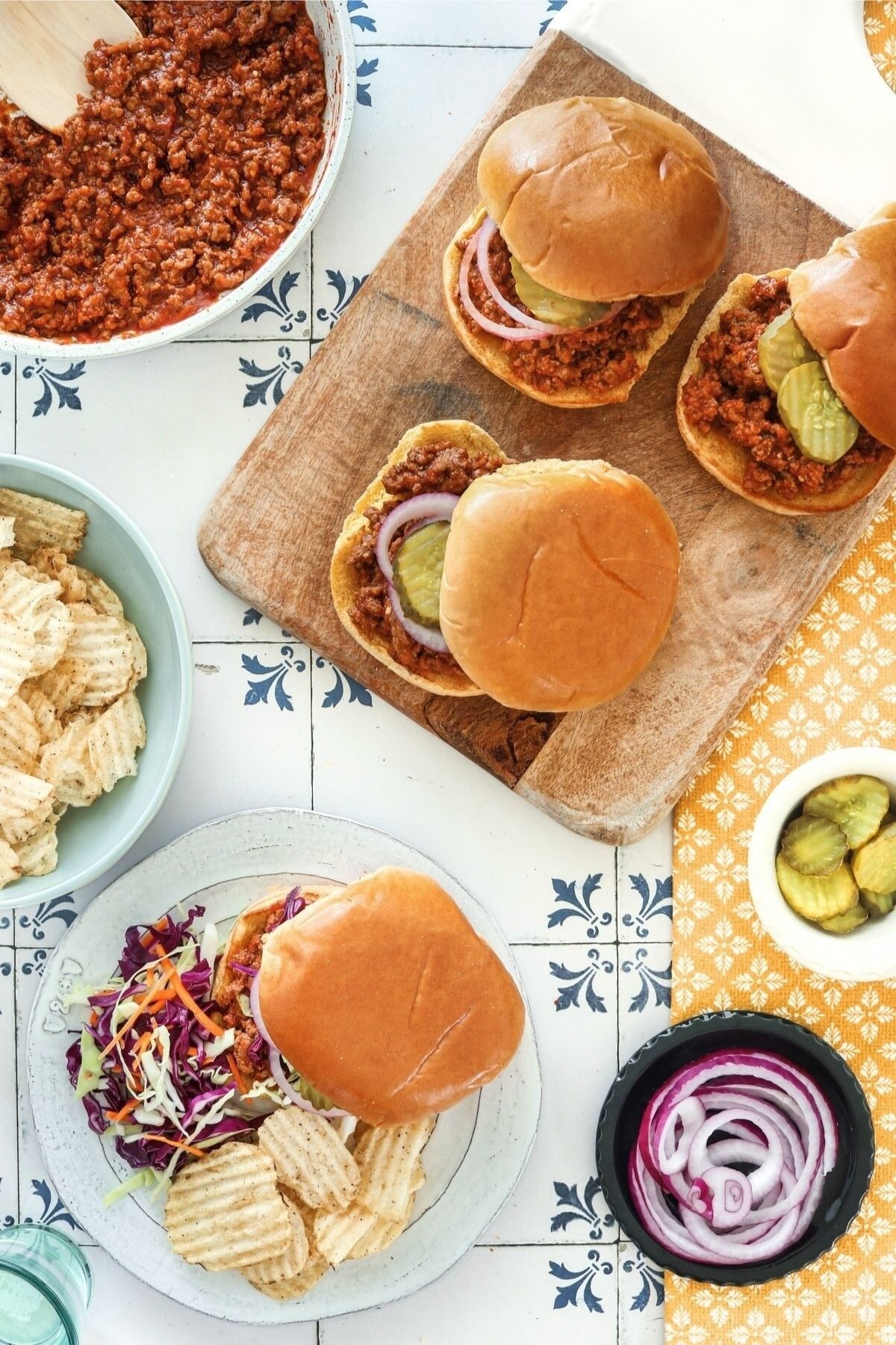 Homemade sloppy joe sandwiches topped with pickles and red onion, served with potato chips and coleslaw.