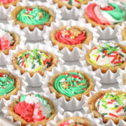 Overhead view of mini chocolate chip cookie cups baked in a mini muffin pan and filled with colorful buttercream frosting and Christmas sprinkles, arranged in white paper cups.