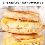 Close-up of two homemade sausage, egg, and cheese English muffin sandwiches stacked on parchment paper, with melted cheese and golden toasted muffins.