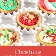 Overhead view of mini chocolate chip cookie cups baked in a mini muffin pan and filled with colorful buttercream frosting and Christmas sprinkles, arranged in white paper cups.