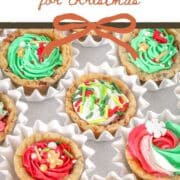 Overhead view of mini chocolate chip cookie cups baked in a mini muffin pan and filled with colorful buttercream frosting and Christmas sprinkles, arranged in white paper cups.