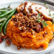 Plated roasted sweet potato casserole topped with a crisp pecan brown sugar streusel, served with sliced roasted turkey and green beans on a white plate.