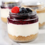 High protein cheesecake jar with a graham cracker crust, creamy cheesecake layer, berry compote topping, and fresh raspberries, blueberries, and blackberries.