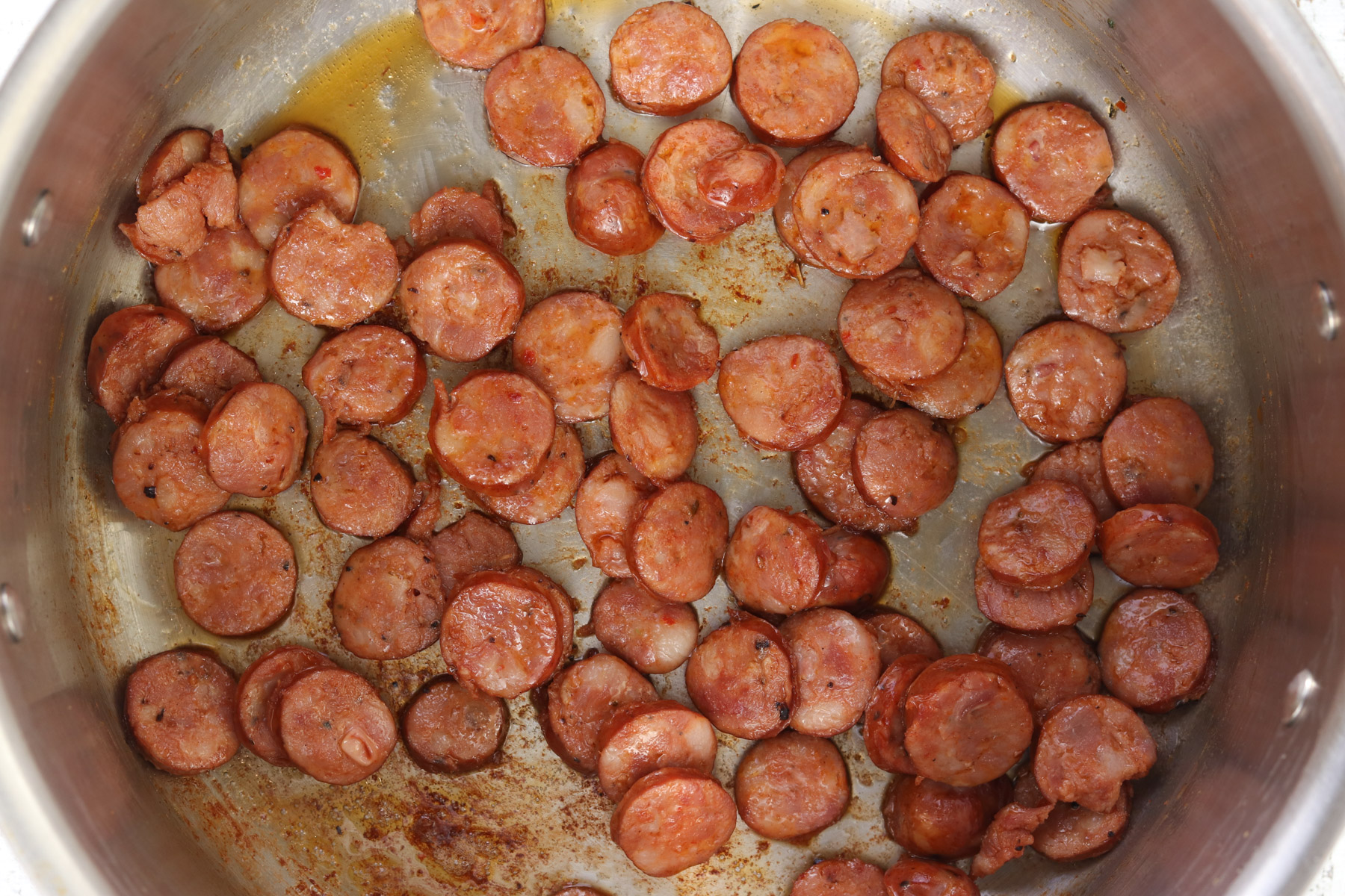 Sliced smoked sausage browning in a large pot with rendered fat and browned bits on the bottom.