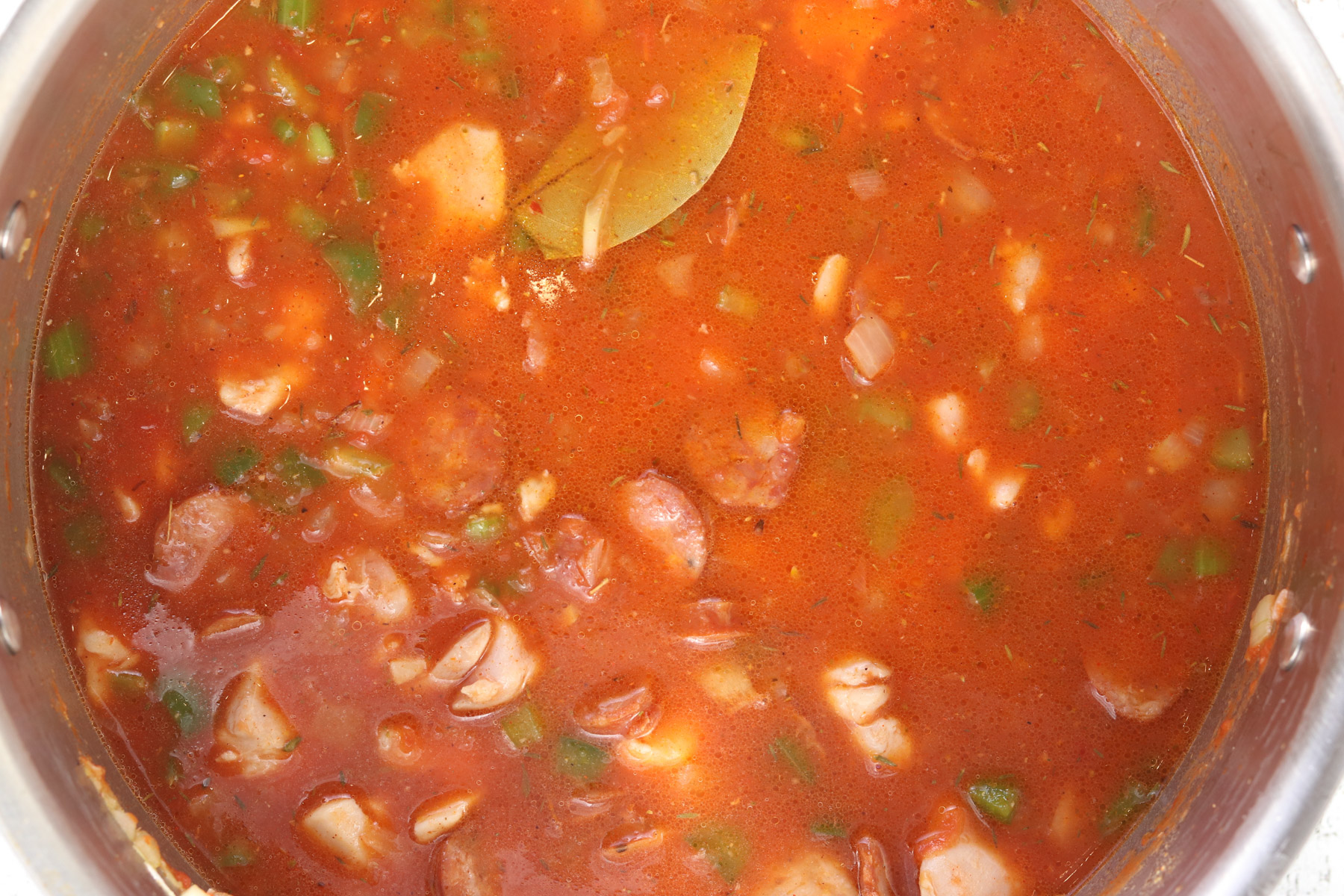 Tomato base added to the pot with chicken, sausage, vegetables, and bay leaf stirred into the broth.