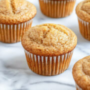 Banana protein muffins in white paper liners on a marble surface, golden brown with domed tops and a soft, tender crumb.