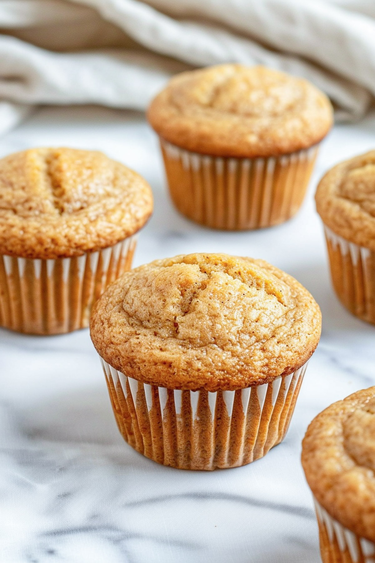 Banana protein muffins in white paper liners on a marble surface, golden brown with domed tops and a soft, tender crumb.