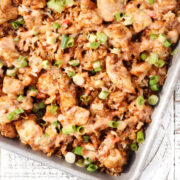 Sheet pan bang bang chicken with crispy rice, featuring roasted chicken pieces tossed with golden rice, drizzled with creamy bang bang sauce, and topped with sliced green onions.