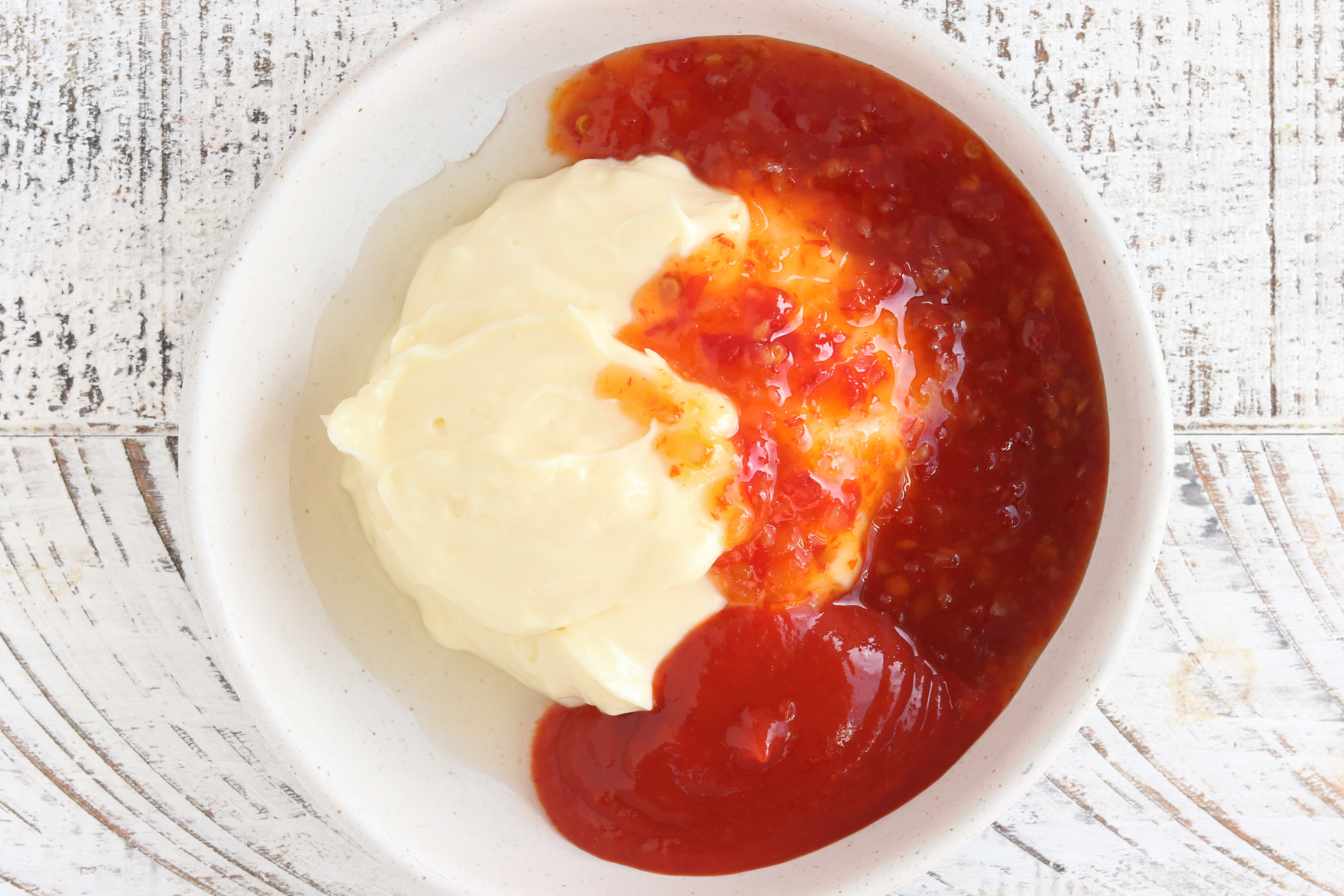 Mayonnaise and sweet chili sauce added to a small bowl, shown before stirring together to make bang bang sauce.