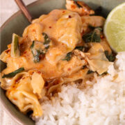 Creamy dumpling bake with shredded chicken and baby bok choy served over white rice, finished with chili crisp and a fresh lime wedge in a shallow bowl.