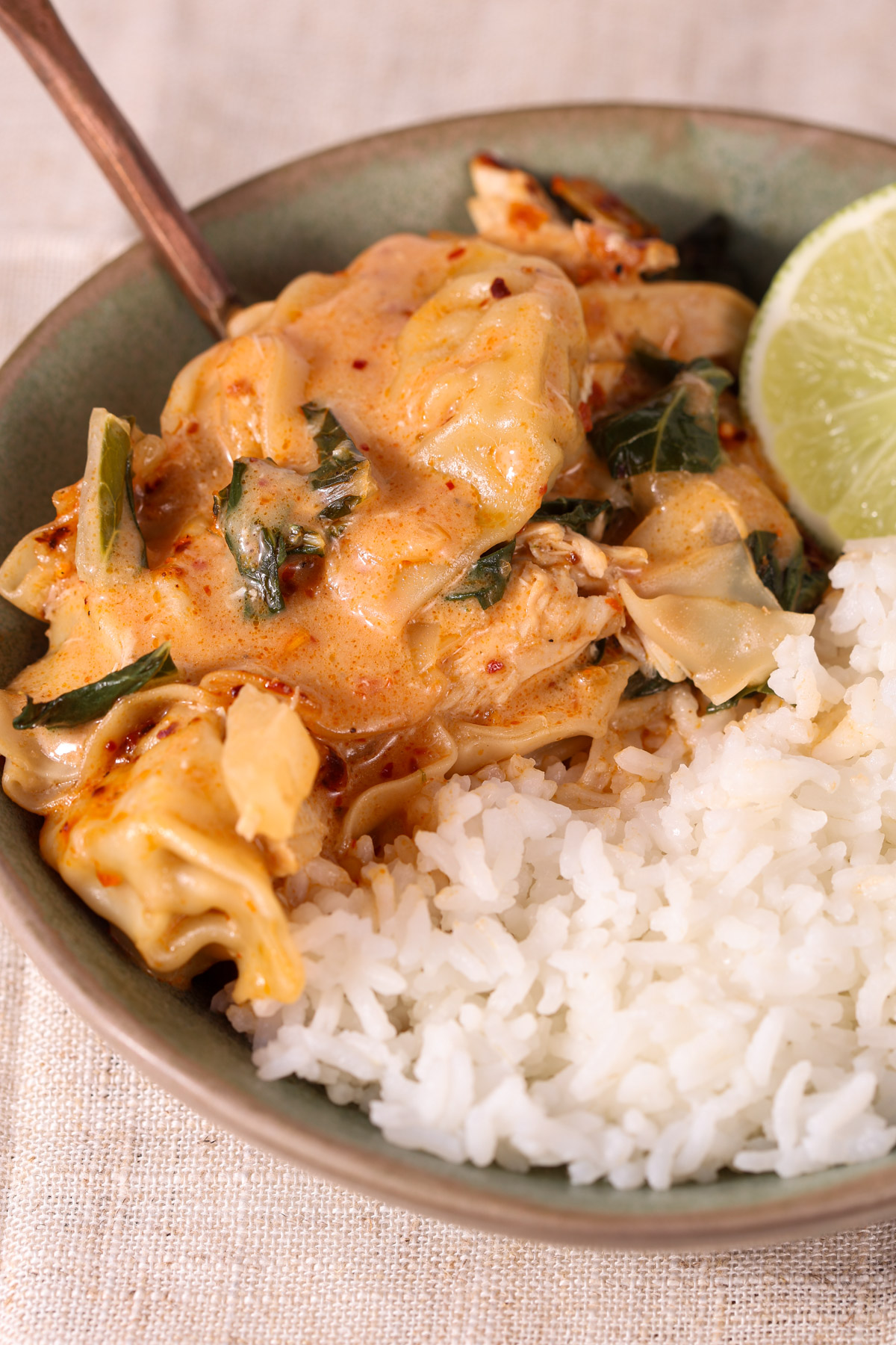 Creamy dumpling bake with shredded chicken and baby bok choy served over white rice, finished with chili crisp and a fresh lime wedge in a shallow bowl.